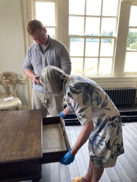 woman in blue gloves examining antique table with man 