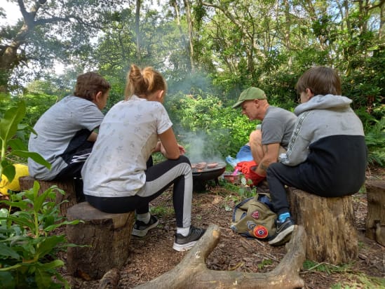 Young people with a youth worker sat around a campfire in the woods